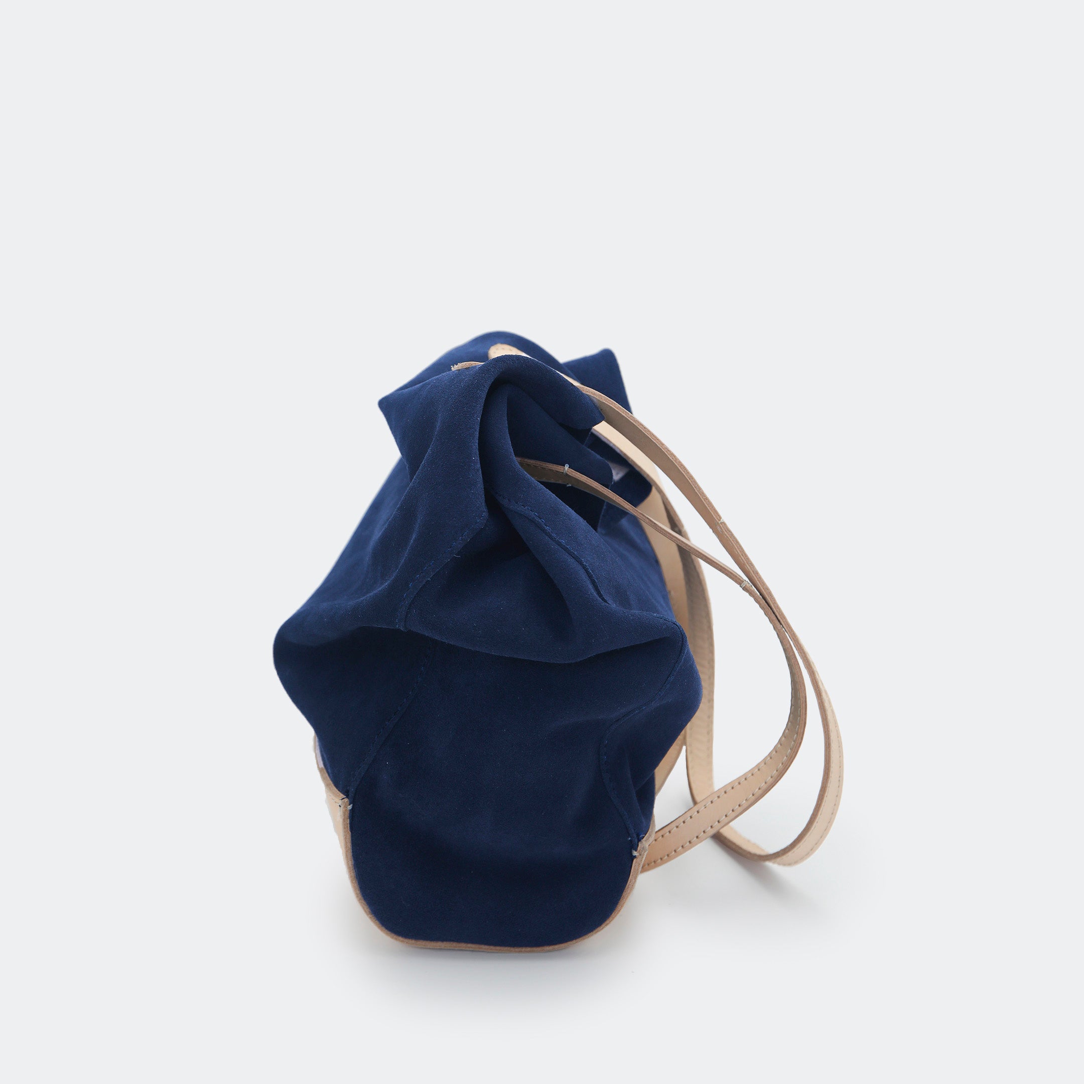 Side view of The Tote Bag in navy blue suede with leather accents, shown relaxed and partially slouched to highlight its soft, unstructured form.