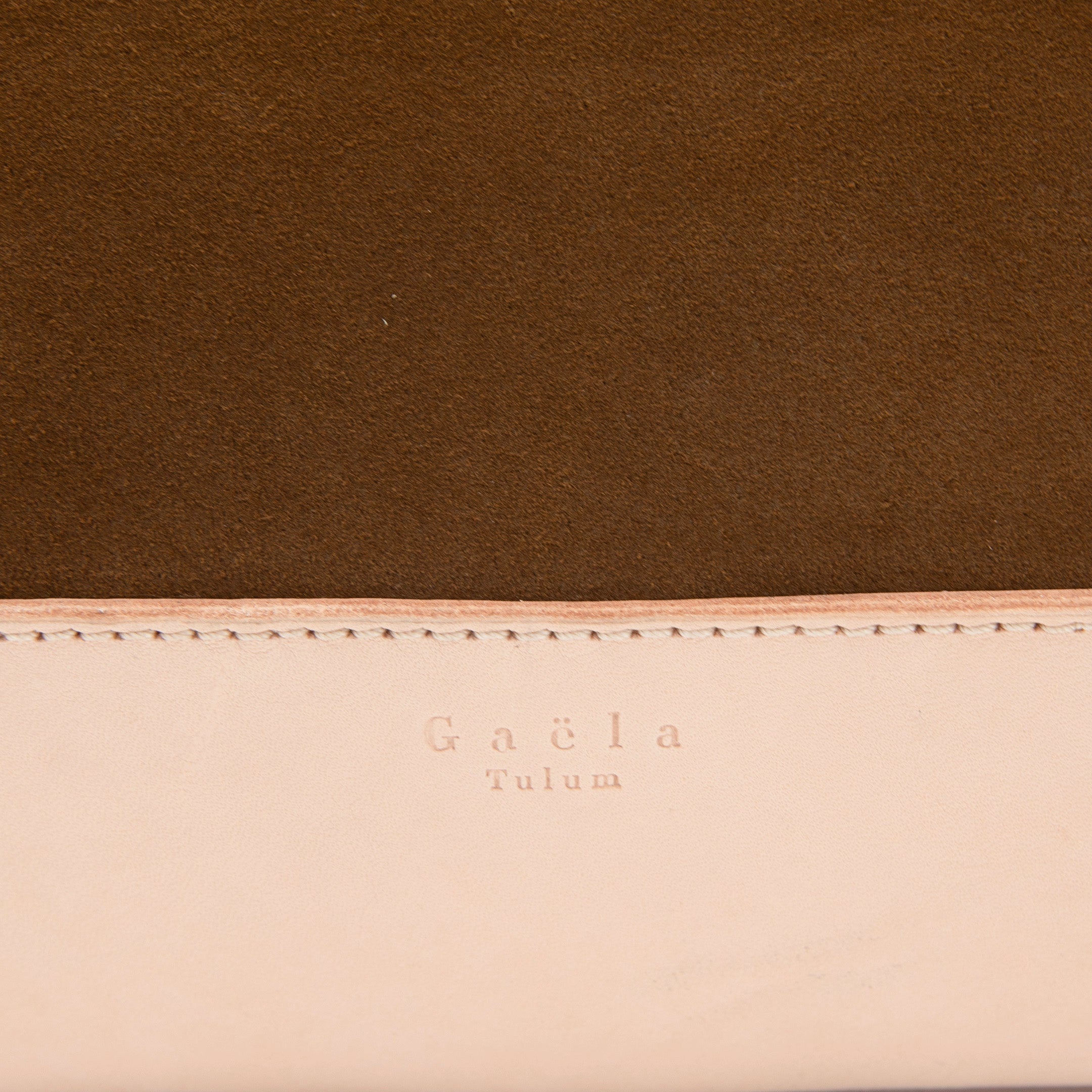 Close-up of The Tote Bag in brown suede, highlighting the texture of the fabric, leather detailing, and visible stitching.