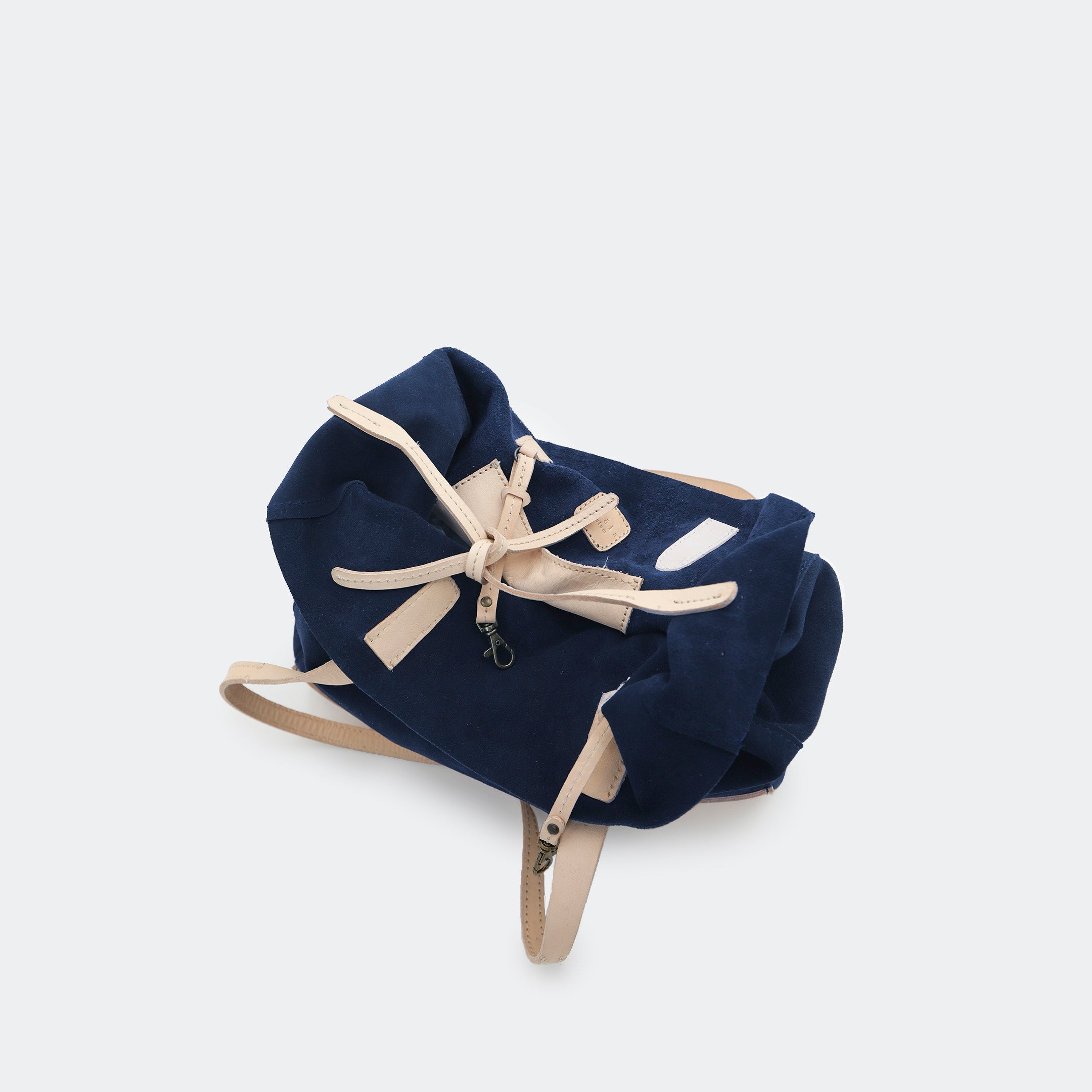 Top-down view of The Tote Bag in navy blue showing tied interior leather straps and visible brass carabiners, with suede and leather interior details highlighted.