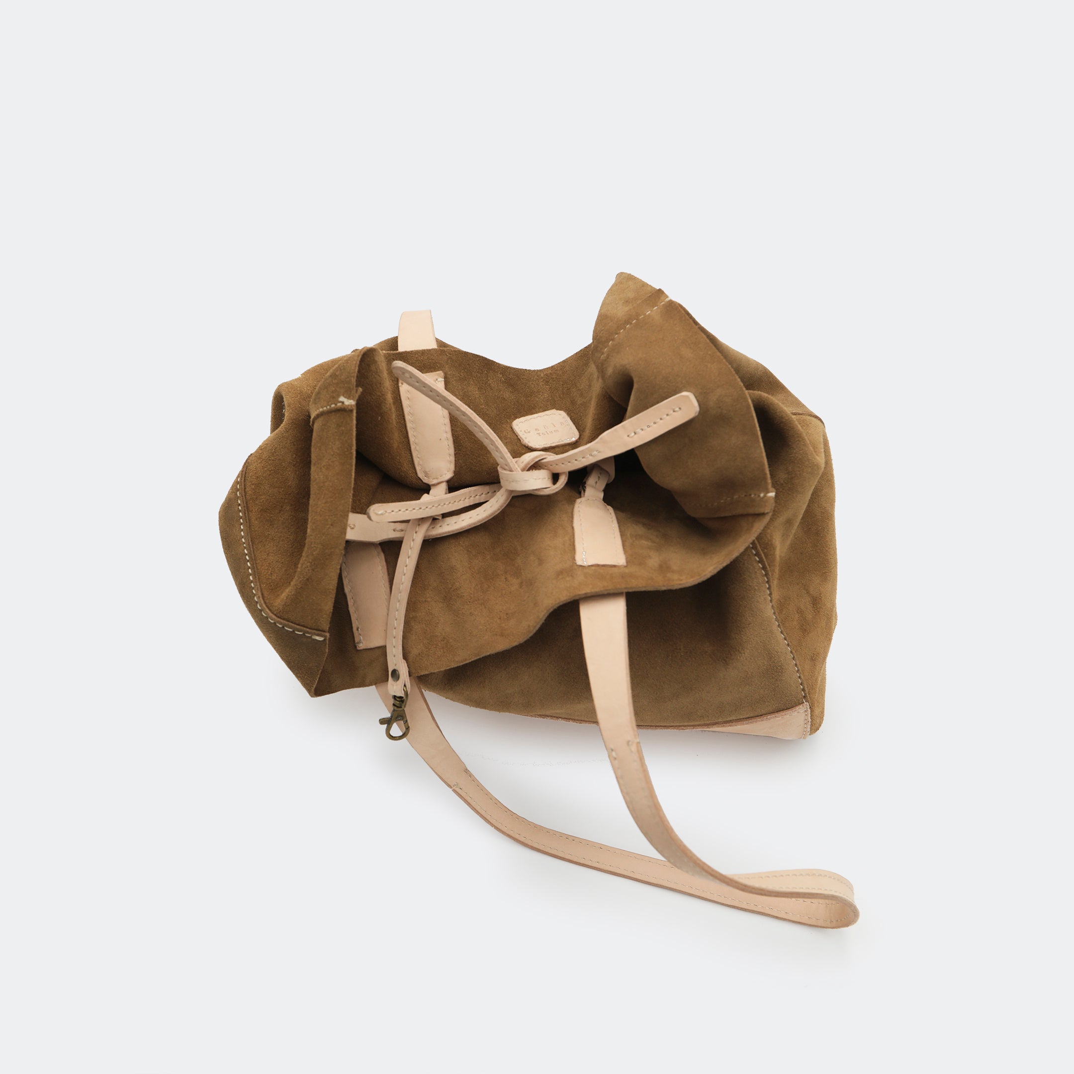 Top-down view of The Tote Bag in brown showing tied interior leather straps and visible brass carabiners, with suede and leather interior details highlighted.