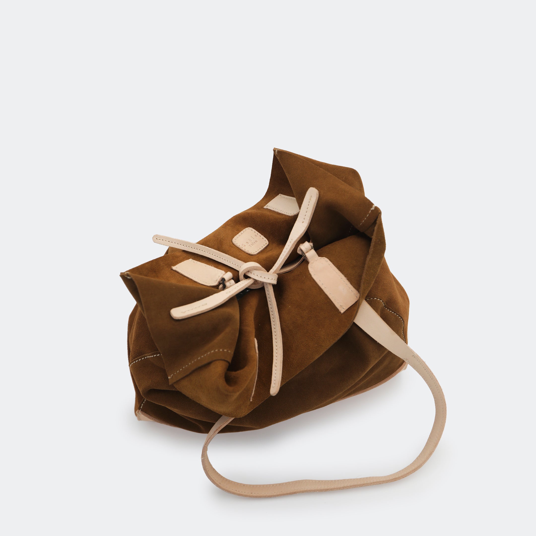 Top-down view of The Tote Bag in brown showing tied interior leather straps and visible brass carabiners, with suede and leather interior details highlighted.