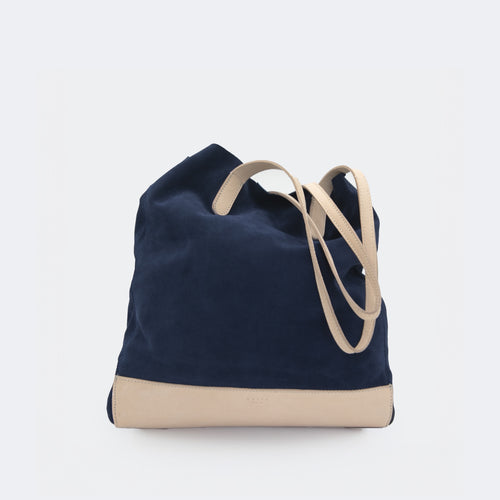 The Tote Bag in navy blue suede with full-grain leather accents on the base and handles, featuring a minimalist silhouette and structured shape.