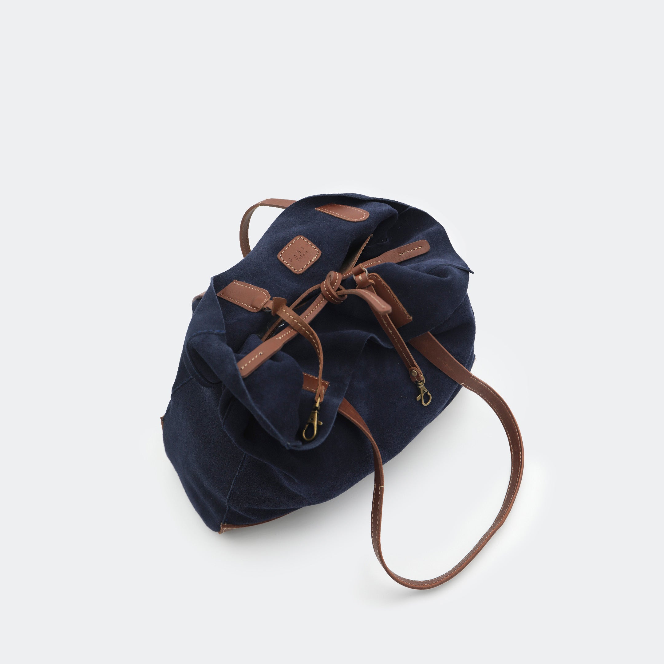 Top-down view of The Tote Bag showing tied interior leather straps and visible brass carabiners, with suede and leather interior details highlighted.