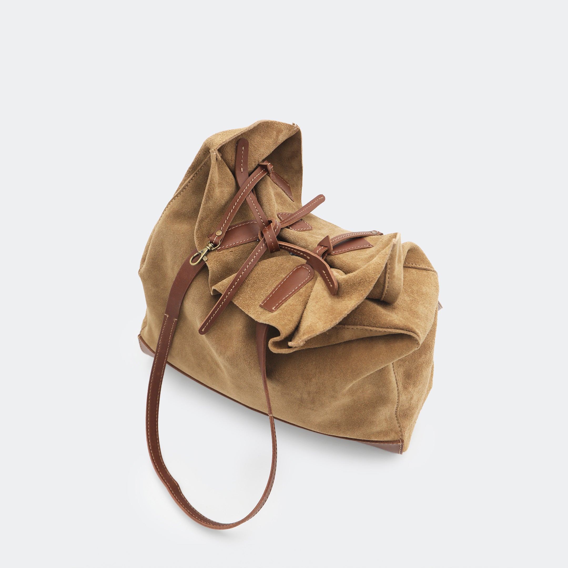 Top-down view of The Tote Bag showing tied interior leather straps and visible brass carabiners, with suede and leather interior details highlighted.