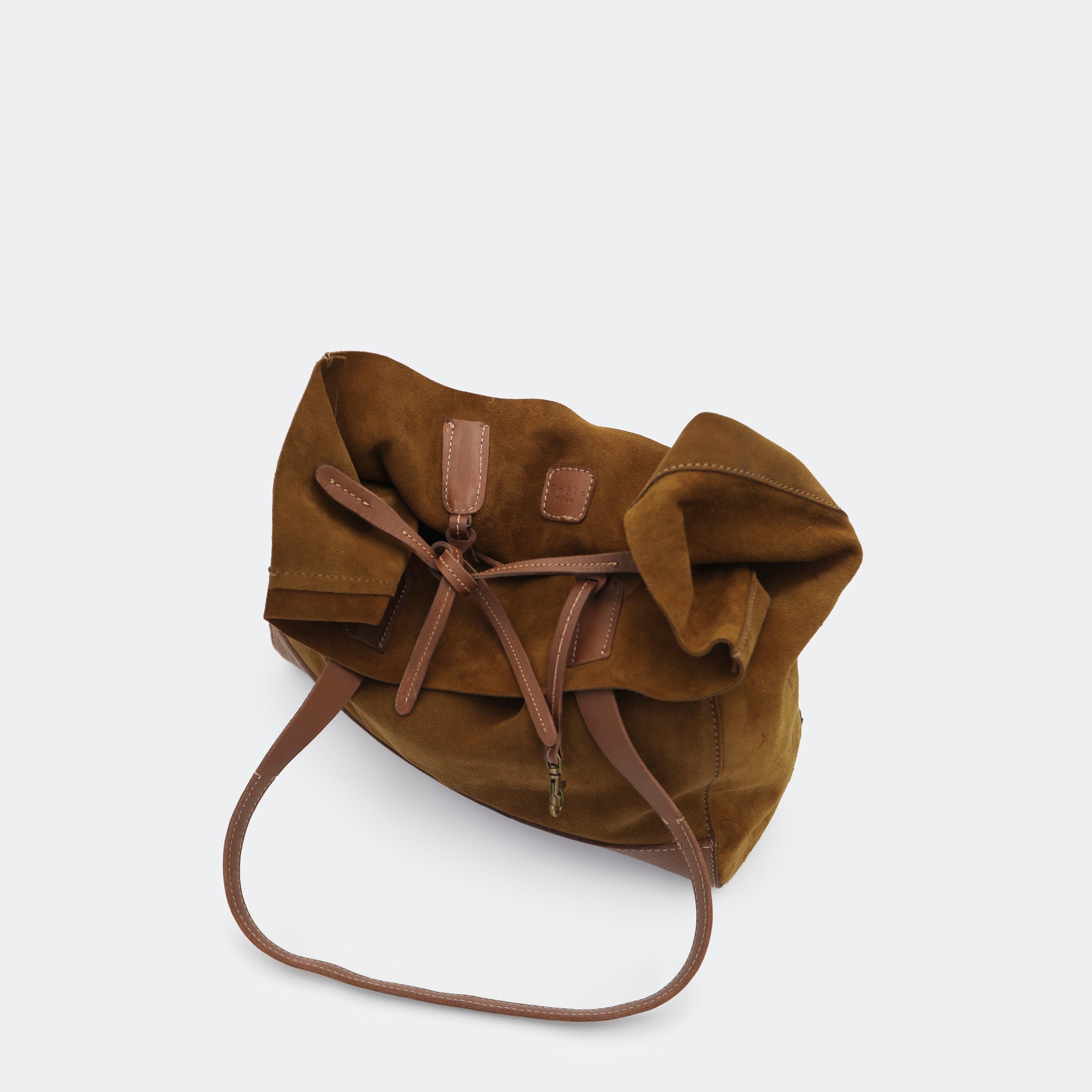 Top-down view of The Tote Bag in brown showing tied interior leather straps and visible brass carabiners, with suede and leather interior details highlighted.