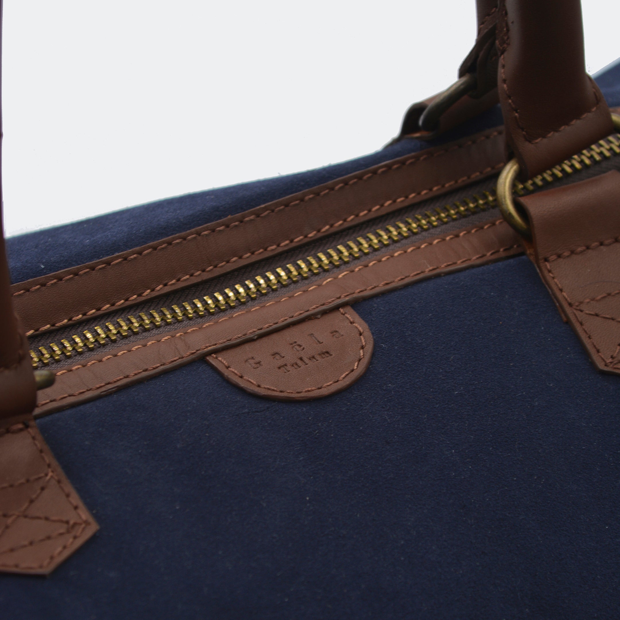 Close-up of The Valise in navy blue leather, showing the curved leather handles, premium hardware, and refined grain texture of the leather.