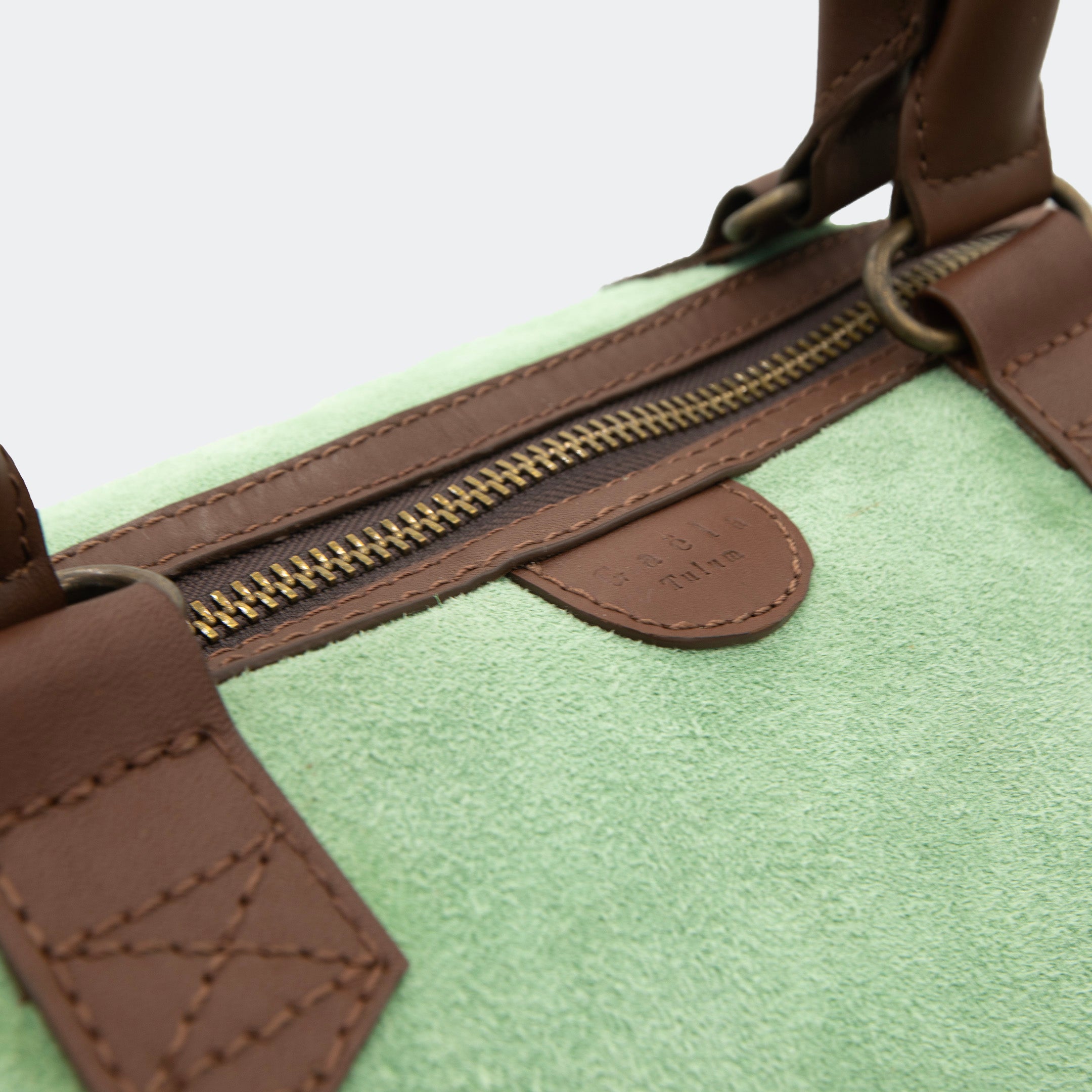 Close-up of The Valise in mint green leather, showing the curved leather handles, premium hardware, and refined grain texture of the leather.