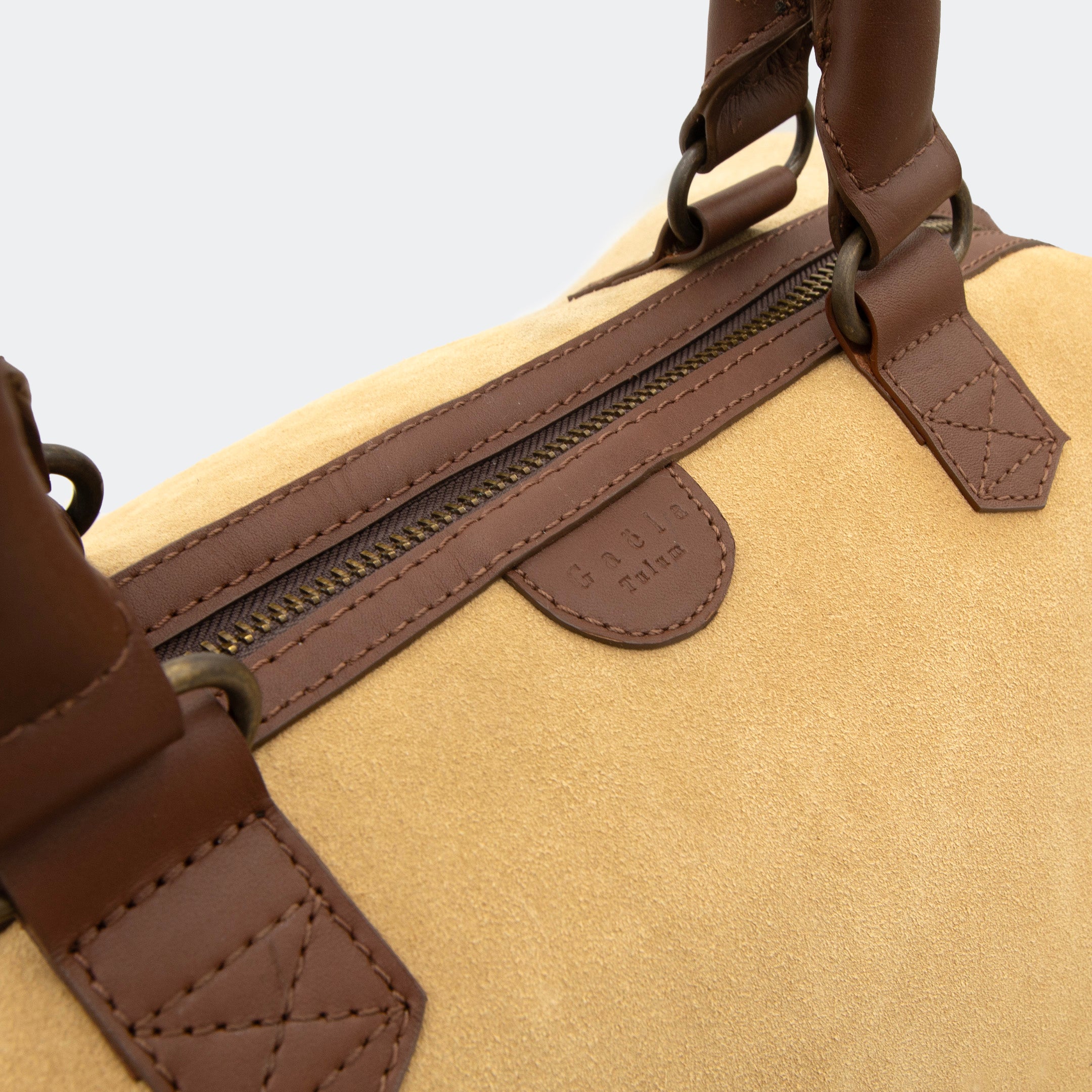 Close-up of The Valise in tan leather, showing the curved leather handles, premium hardware, and refined grain texture of the leather.