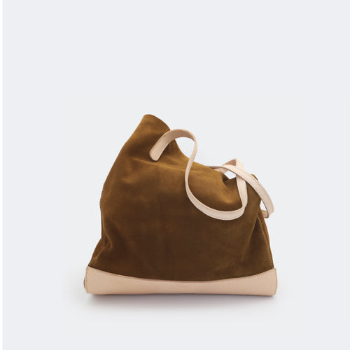 The Tote Bag in brown suede with full-grain leather accents on the base and handles, featuring a minimalist silhouette and structured shape.
