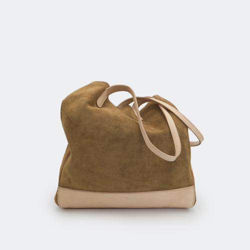The Tote Bag in brown suede with full-grain leather accents on the base and handles, featuring a minimalist silhouette and structured shape.