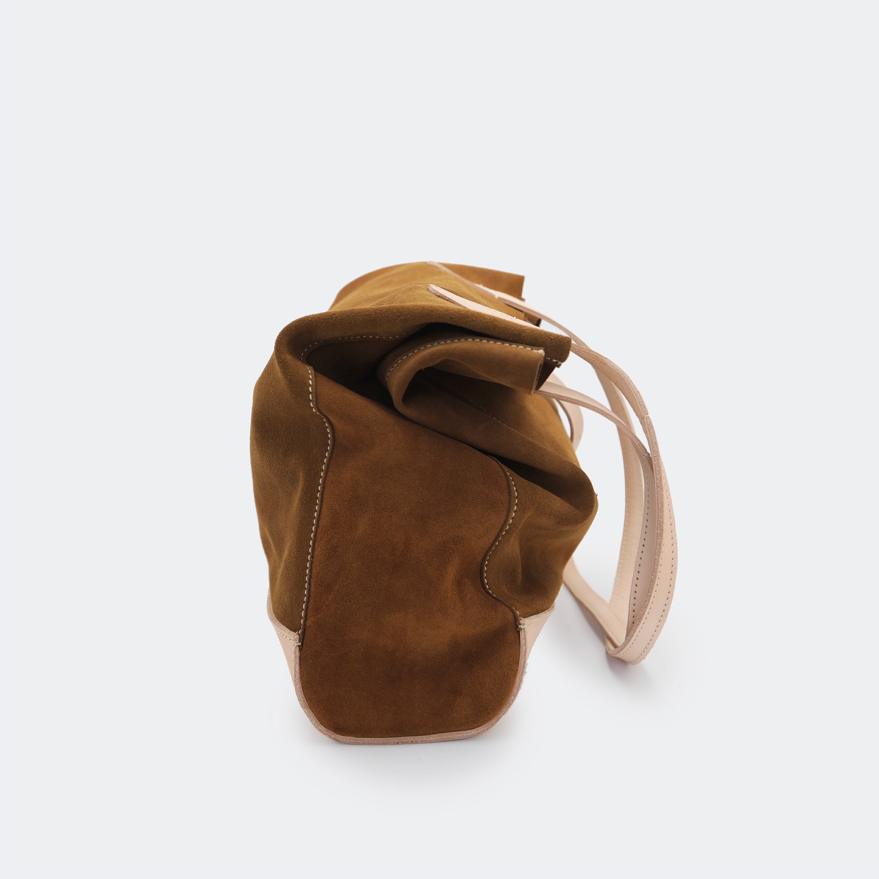 Side view of The Tote Bag in brown suede with leather accents, shown relaxed and partially slouched to highlight its soft, unstructured form.