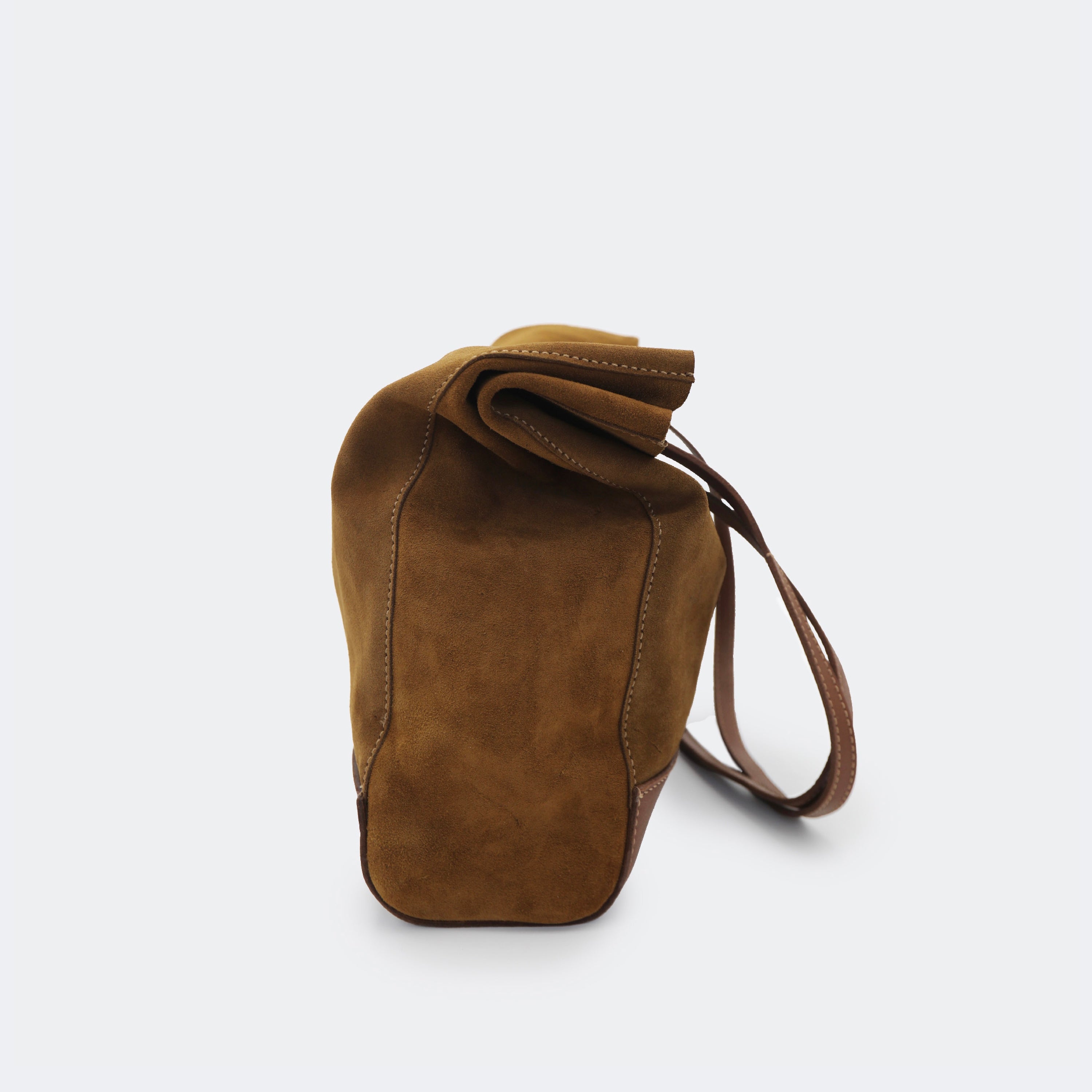 Side view of The Tote Bag in brown suede with leather accents, shown relaxed and partially slouched to highlight its soft, unstructured form.
