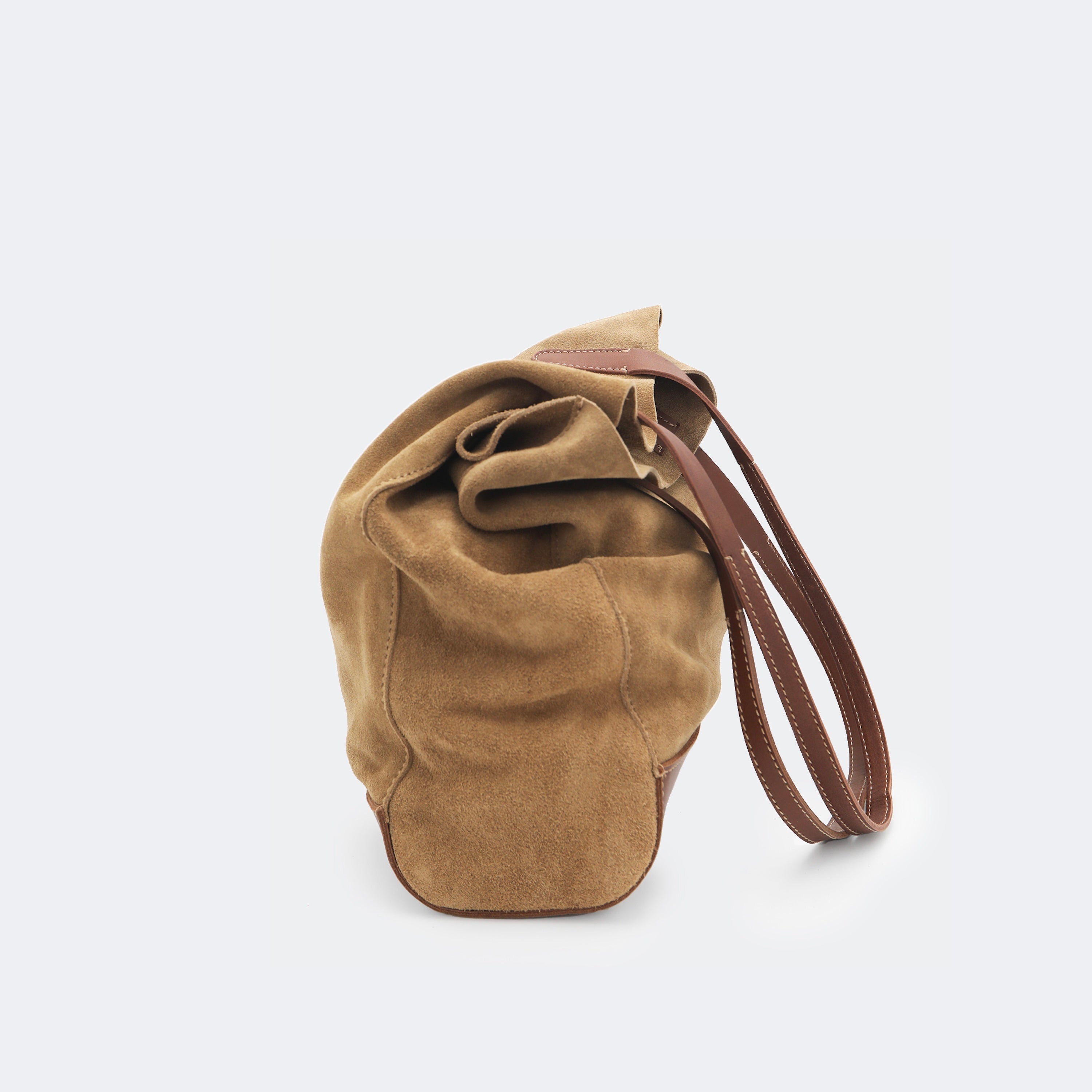 Side view of The Tote Bag in brown suede with leather accents, shown relaxed and partially slouched to highlight its soft, unstructured form.
