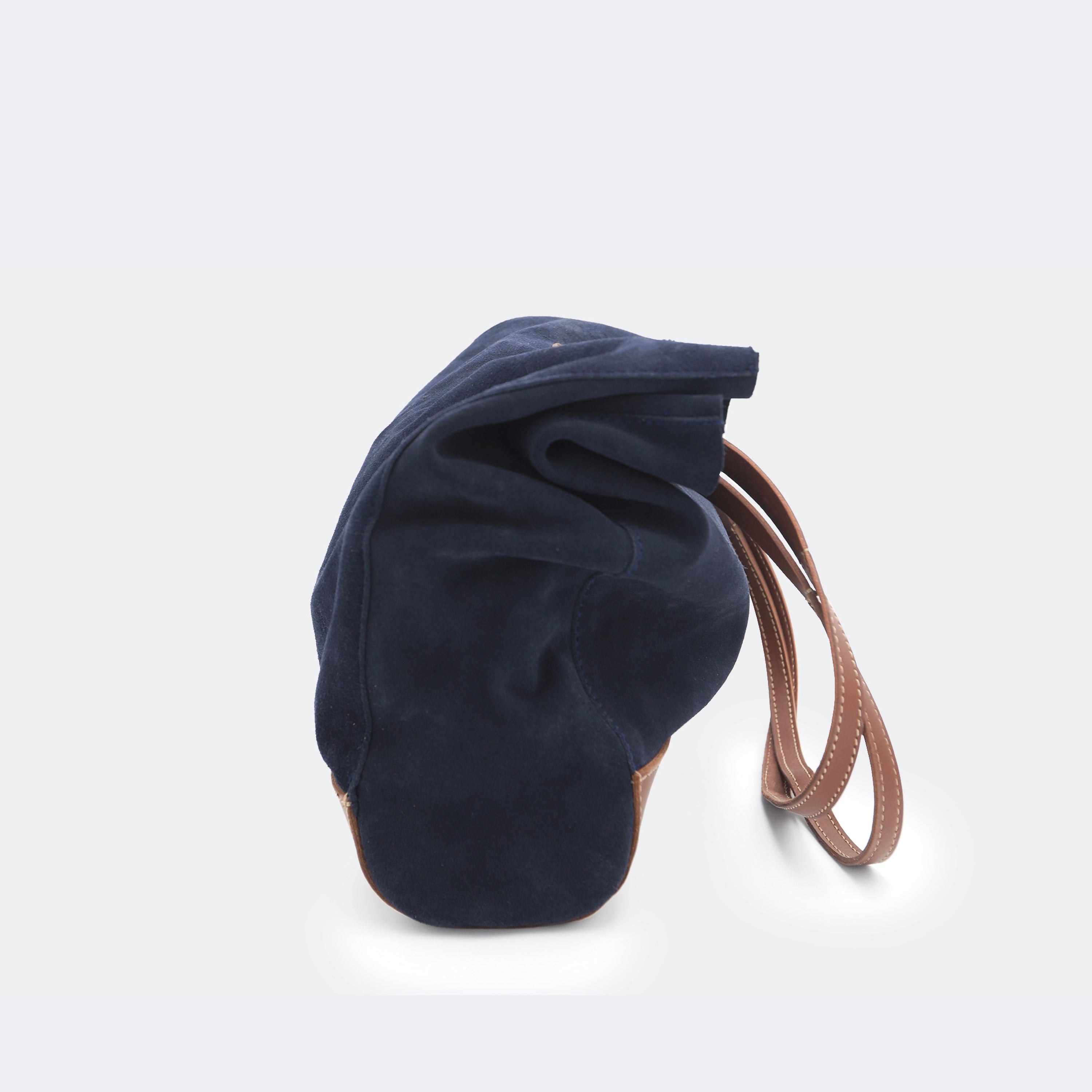Side view of The Tote Bag in navy suede with brown leather accents, shown relaxed and partially slouched to highlight its soft, unstructured form.