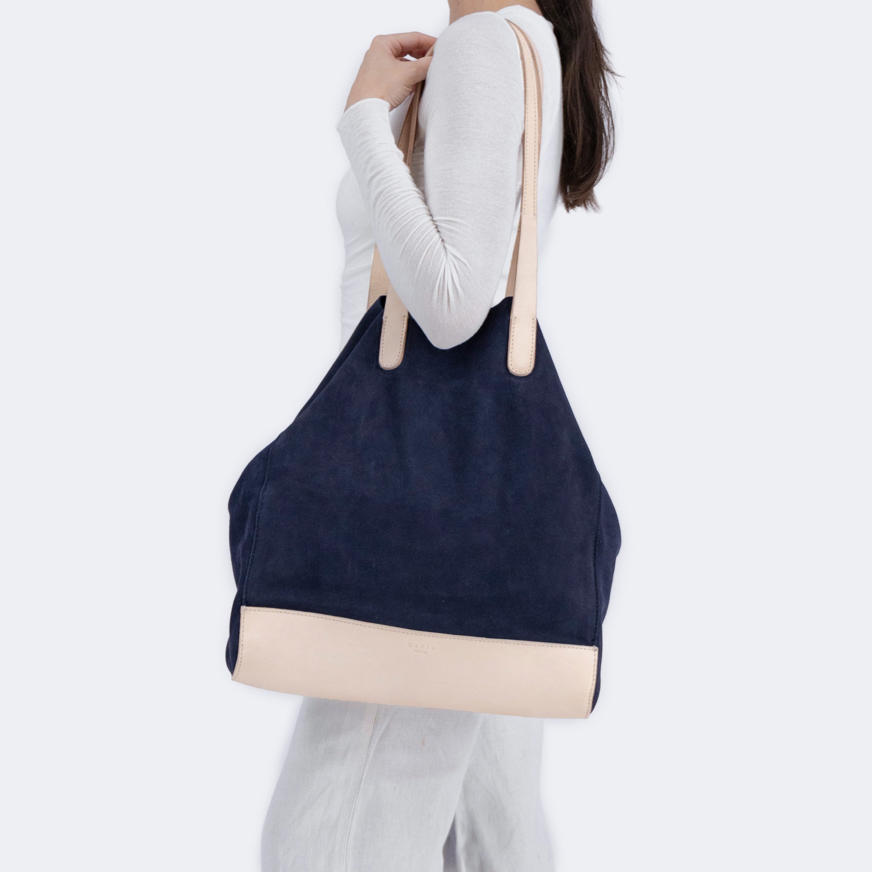 Model carrying The Tote Bag in navy blue suede with leather accents, showcasing its soft structure and minimalist design.