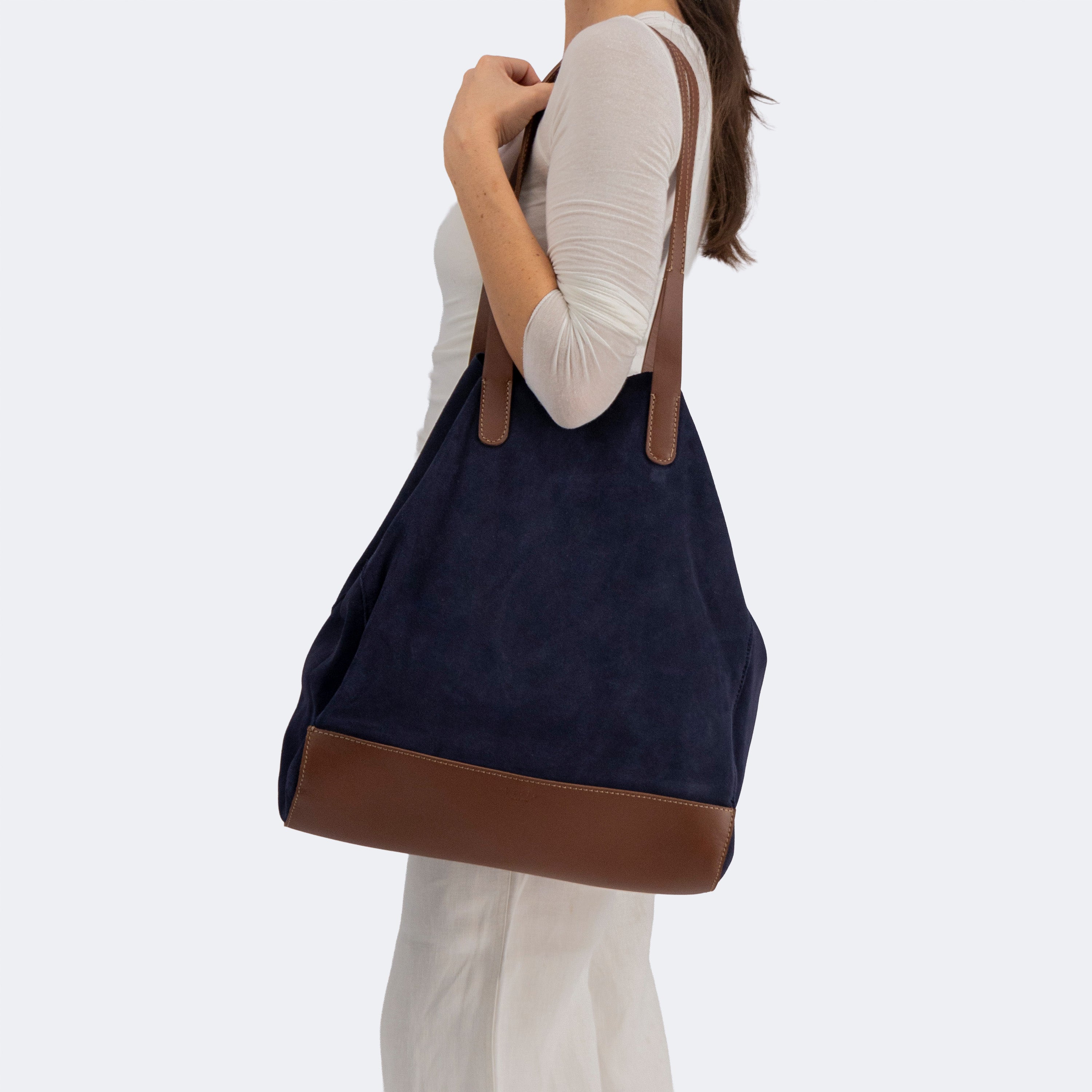 Model carrying The Tote Bag in navy suede with brown leather accents, showcasing its soft structure and minimalist design.