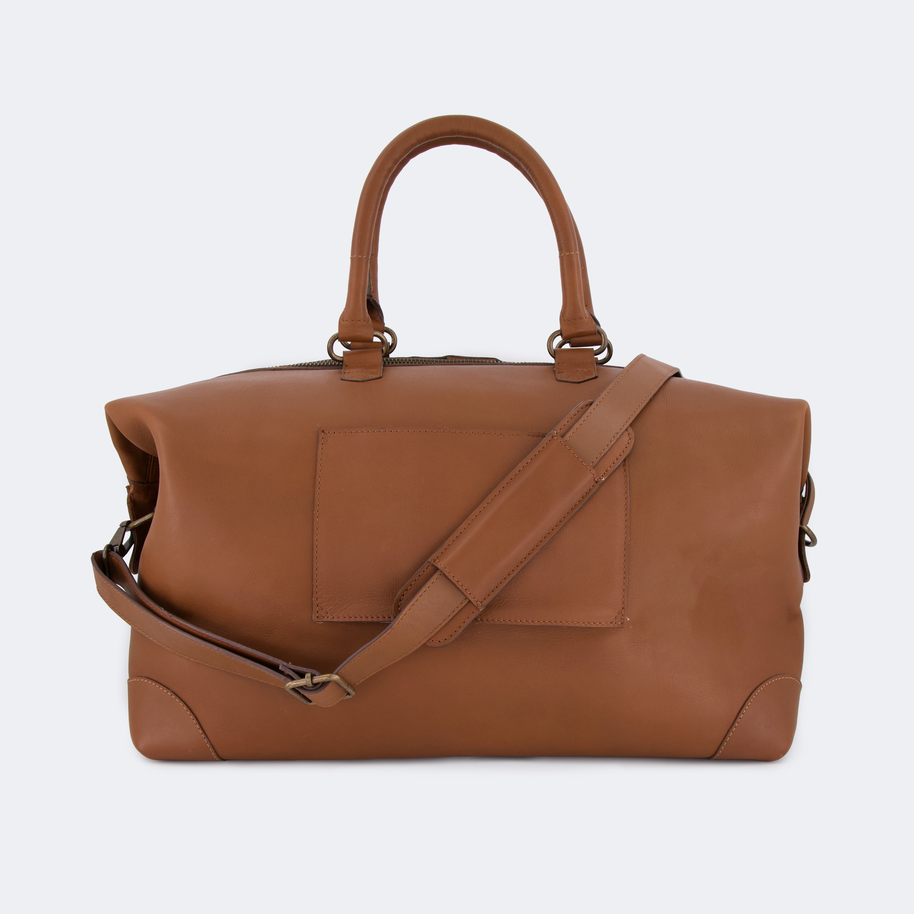 The Valise in brown leather shown from behind, highlighting the integrated luggage band designed to slide over a suitcase handle.