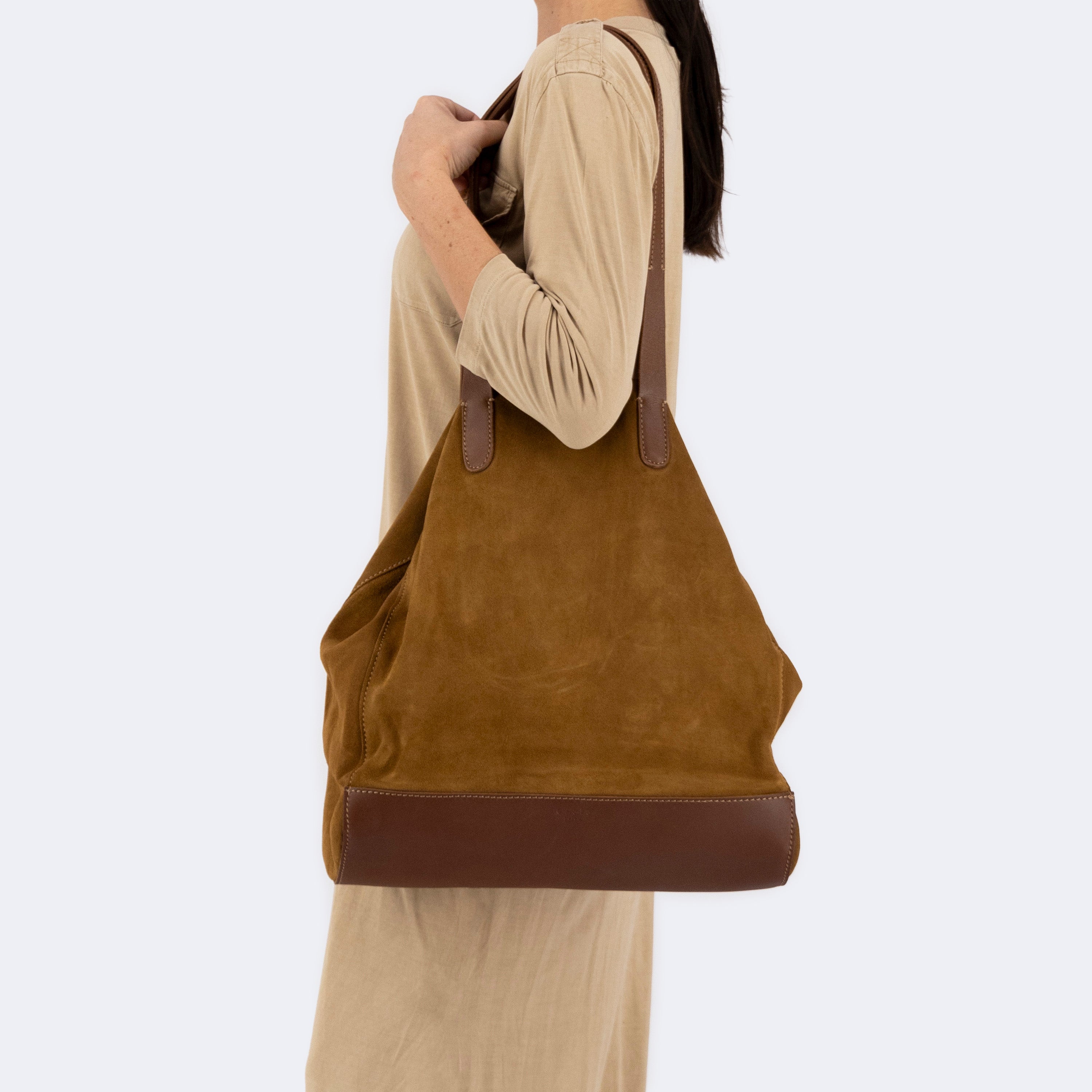 Model carrying The Tote Bag in brown suede with leather accents, showcasing its soft structure and minimalist design.