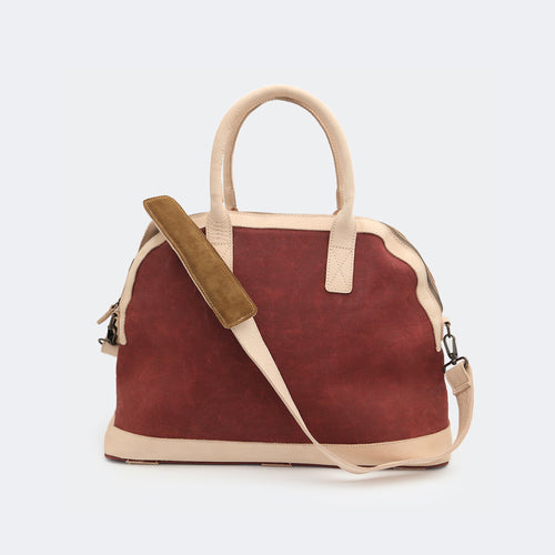 The Weekender in wine red, shown with its removable leather shoulder strap attached — designed for comfortable, hands-free travel.