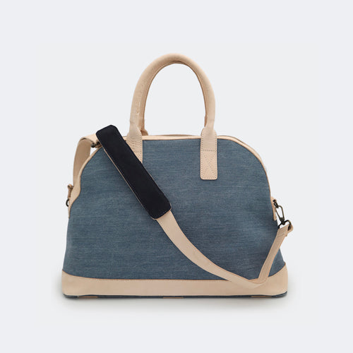 The Weekender in denim, shown with its removable leather shoulder strap attached — designed for comfortable, hands-free travel.