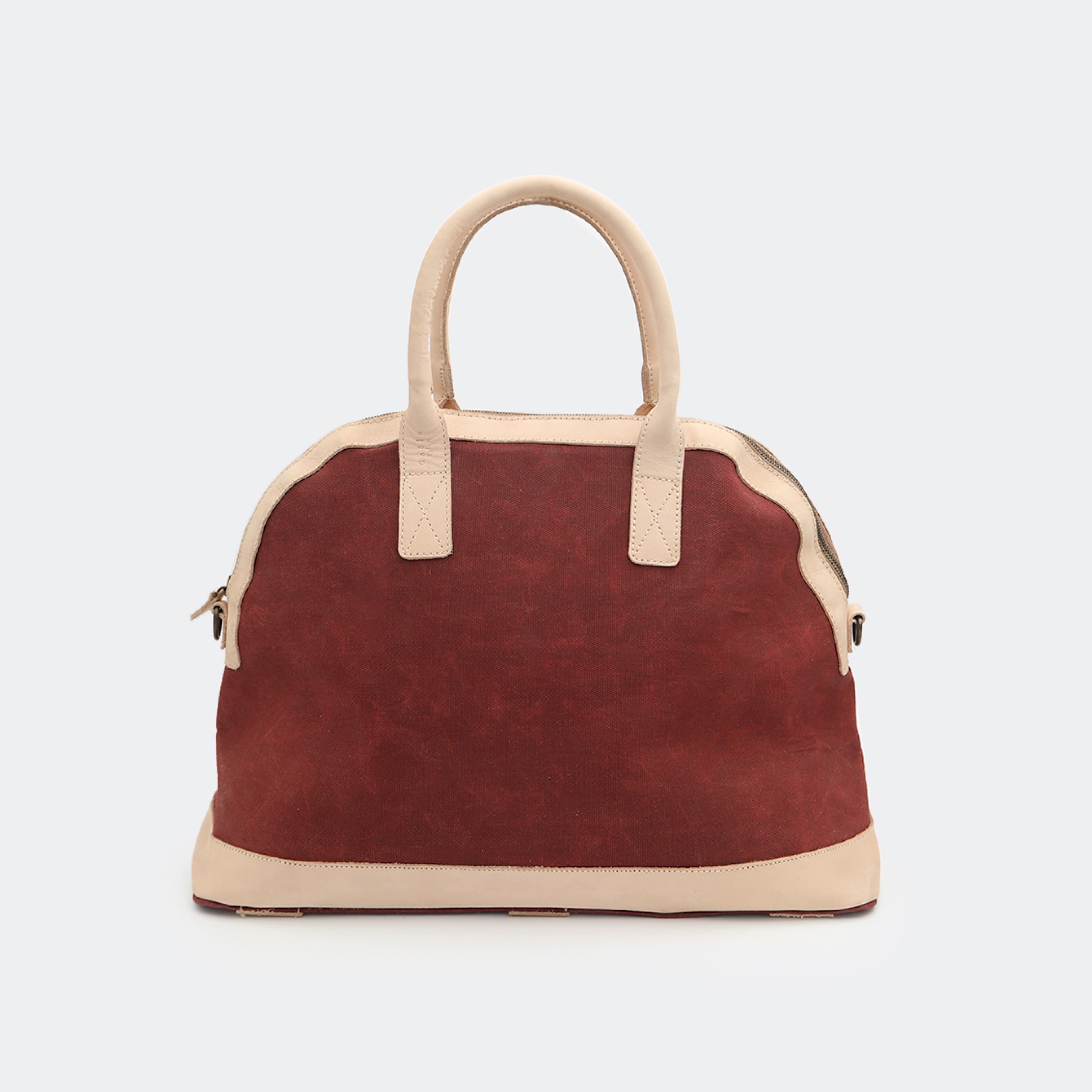 The Weekender in wine red, crafted from waxed cotton with full-grain leather accents — a spacious travel bag with a clean silhouette and curved handles.