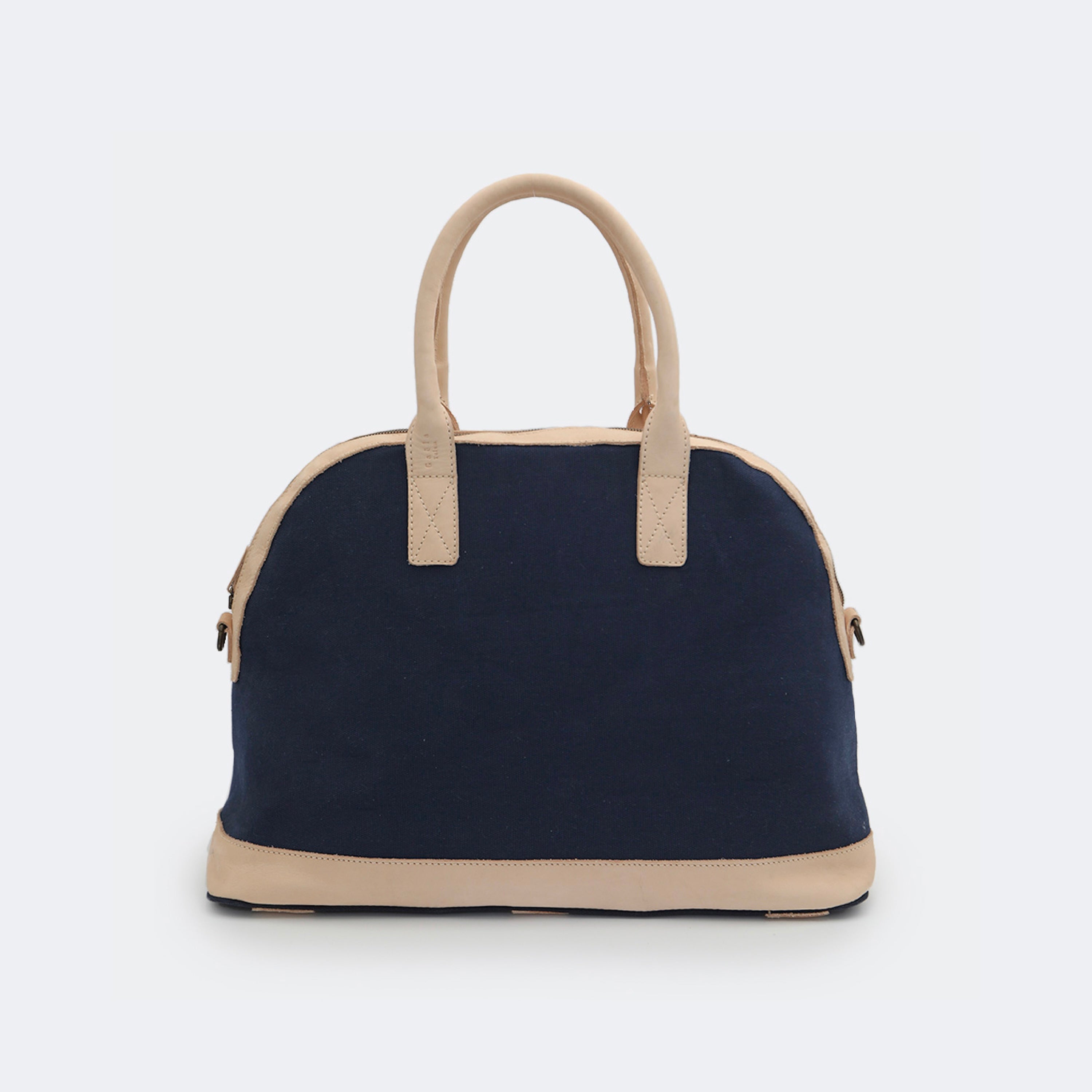 The Weekender in navy blue, crafted from cotton with full-grain leather accents — a spacious travel bag with a clean silhouette and curved handles.
