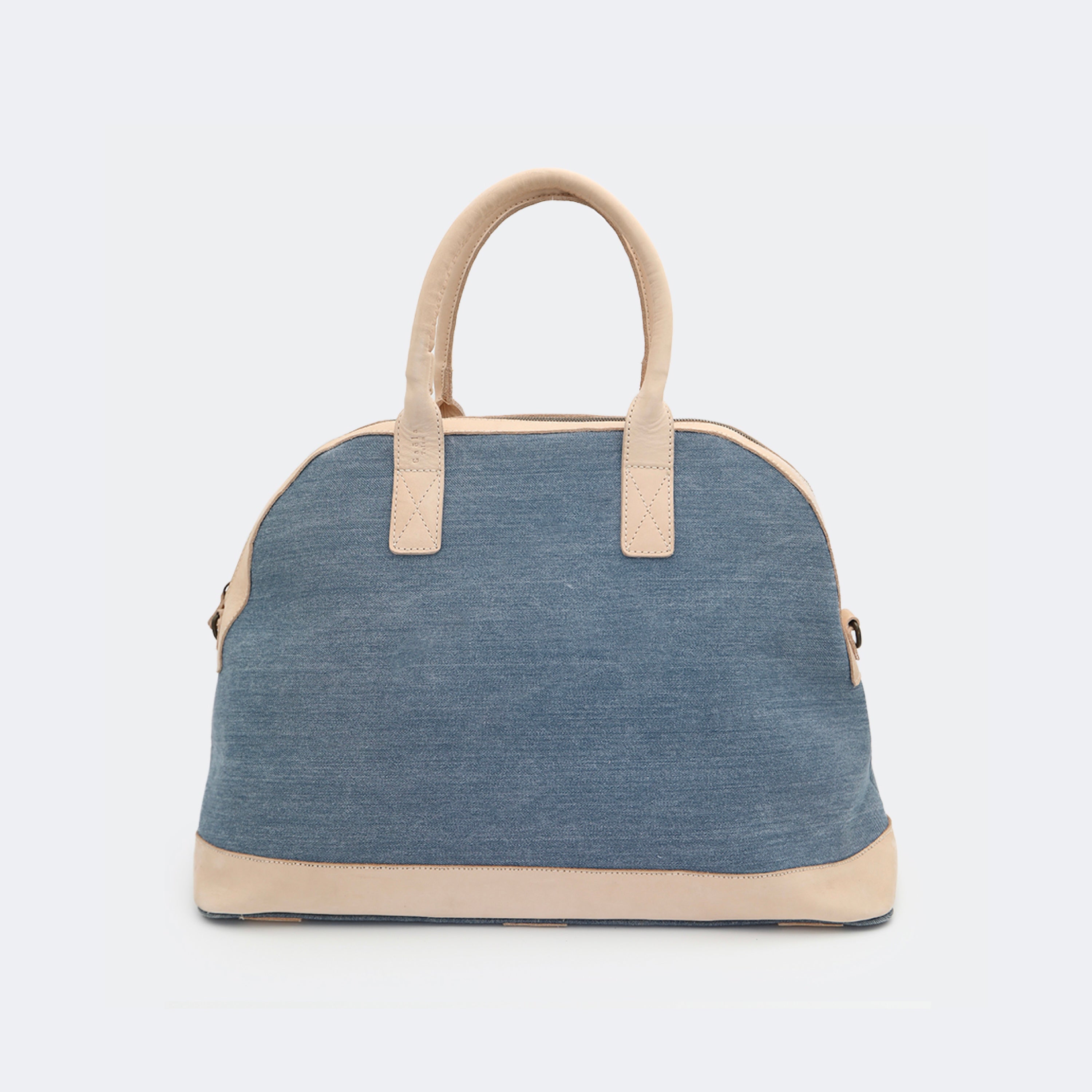 The Weekender in denim, crafted from cotton with full-grain leather accents — a spacious travel bag with a clean silhouette and curved handles.