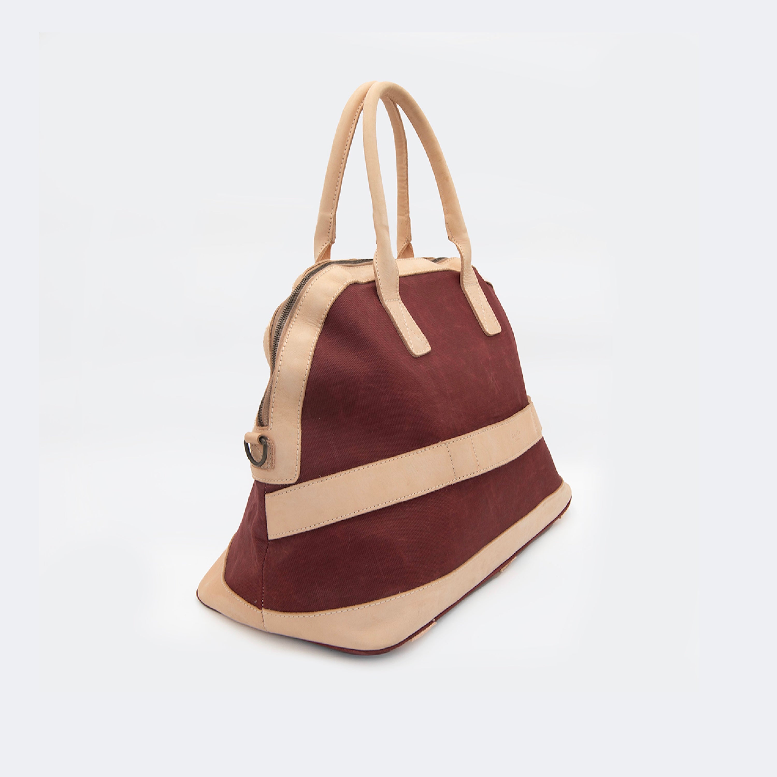 The Weekender in wine red, crafted from waxed cotton with full-grain leather accents — a spacious travel bag with a clean silhouette and curved handles.