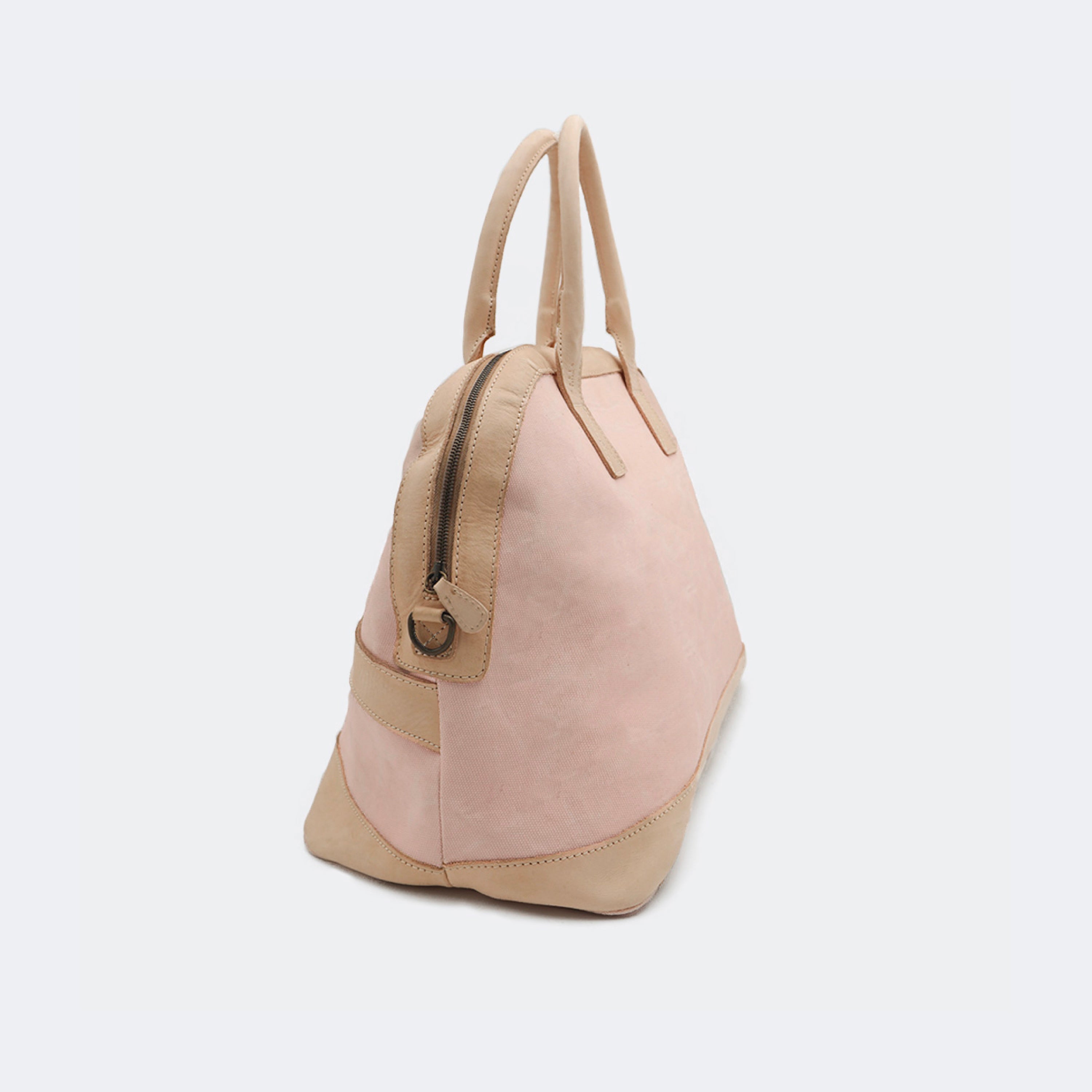 The Weekender in blush pink, crafted from waxed cotton with full-grain leather accents — a spacious travel bag with a clean silhouette and curved handles.