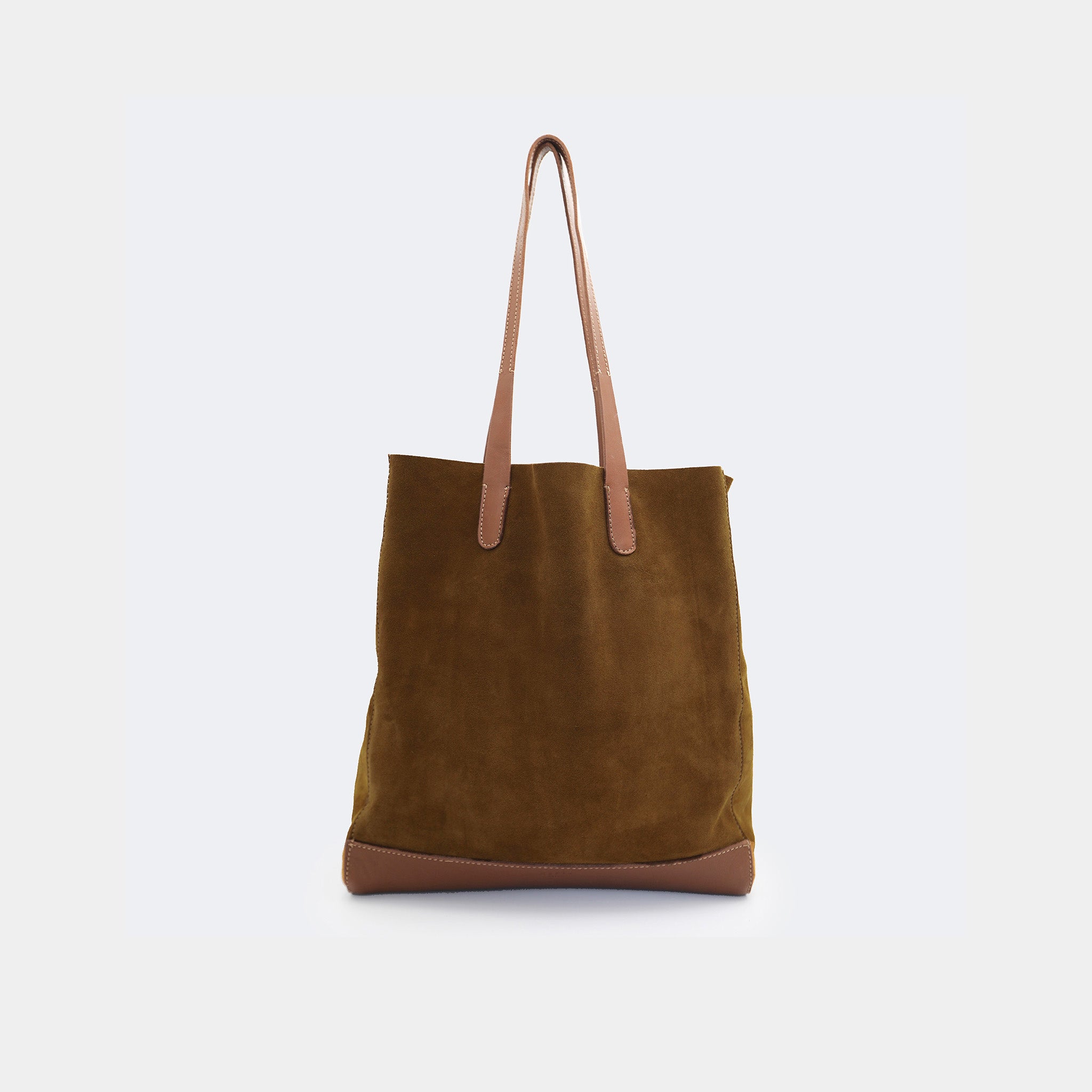 The Tote Bag in brown suede with full-grain leather accents on the base and handles, featuring a minimalist silhouette and structured shape.